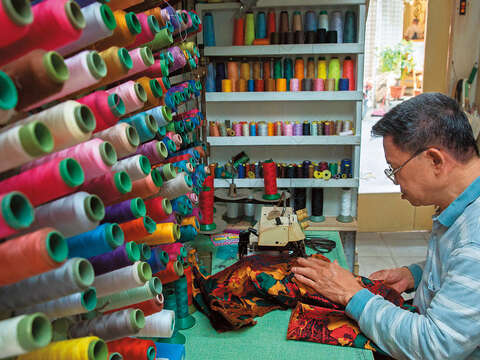 陳忠信用針線縫製美麗旗袍，而這些彩色針線也織就他的人生。（攝影／林煒凱）