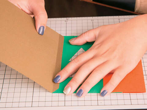 Step4 將綠色美術紙翻到背面，將咖啡色美術紙左邊內摺1cm，內摺處黏貼於綠色美術紙右方，並向左摺，覆蓋於綠色與橘紅色美術紙。（攝影／賴智揚）
