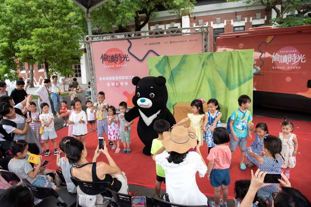 北市图行动书车邀请爱看书的超人气熊赞代言行动书车，照片为书车启动仪式中，人气满满的熊赞邀请在场小朋友一起大合照