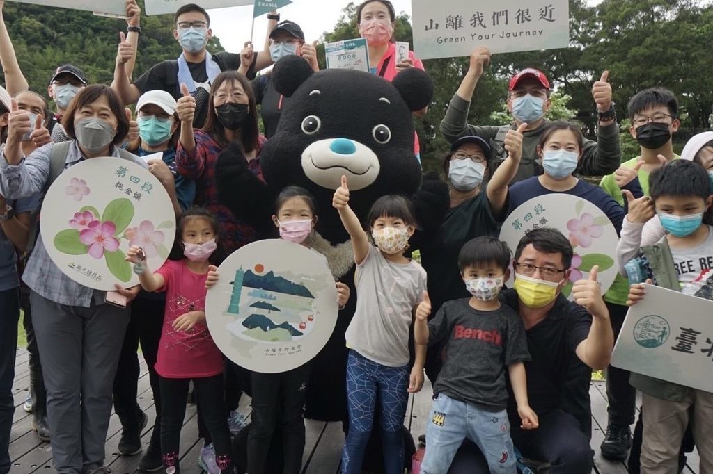 北市观传局副局长李丽珠与吉祥物熊赞现身「台北大纵走7 1段系列活动」第四场体验活动，颁发完走证书及登山扣环给参与民众。