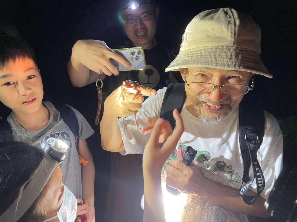 富阳公园蛙调志工郭水源老师在让小朋友们轮流体验蛙类吸盘的黏着力，接着示范如何将斑腿树蛙装入网袋，进行移除外来种的作业。(图片来源：台北市政府观光传播局)